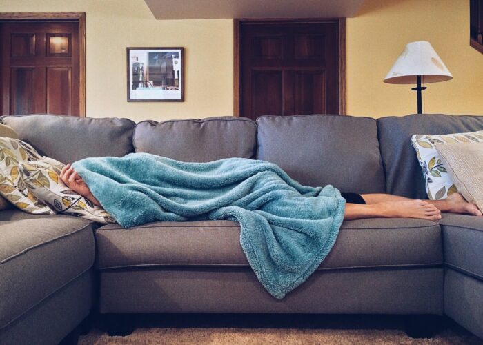 Image of woman lying on a couch, her face and upper body covered by a blanket. 