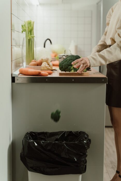 Woman throwing a piece of broccoli into her kitchen trash can. 