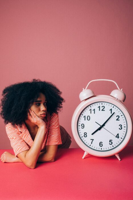 Why goals suck: because they cause you to delay happiness. 

Pic: Woman staring at a large pink clock. She's against a pink background and wearing an orange and white striped jacket. 